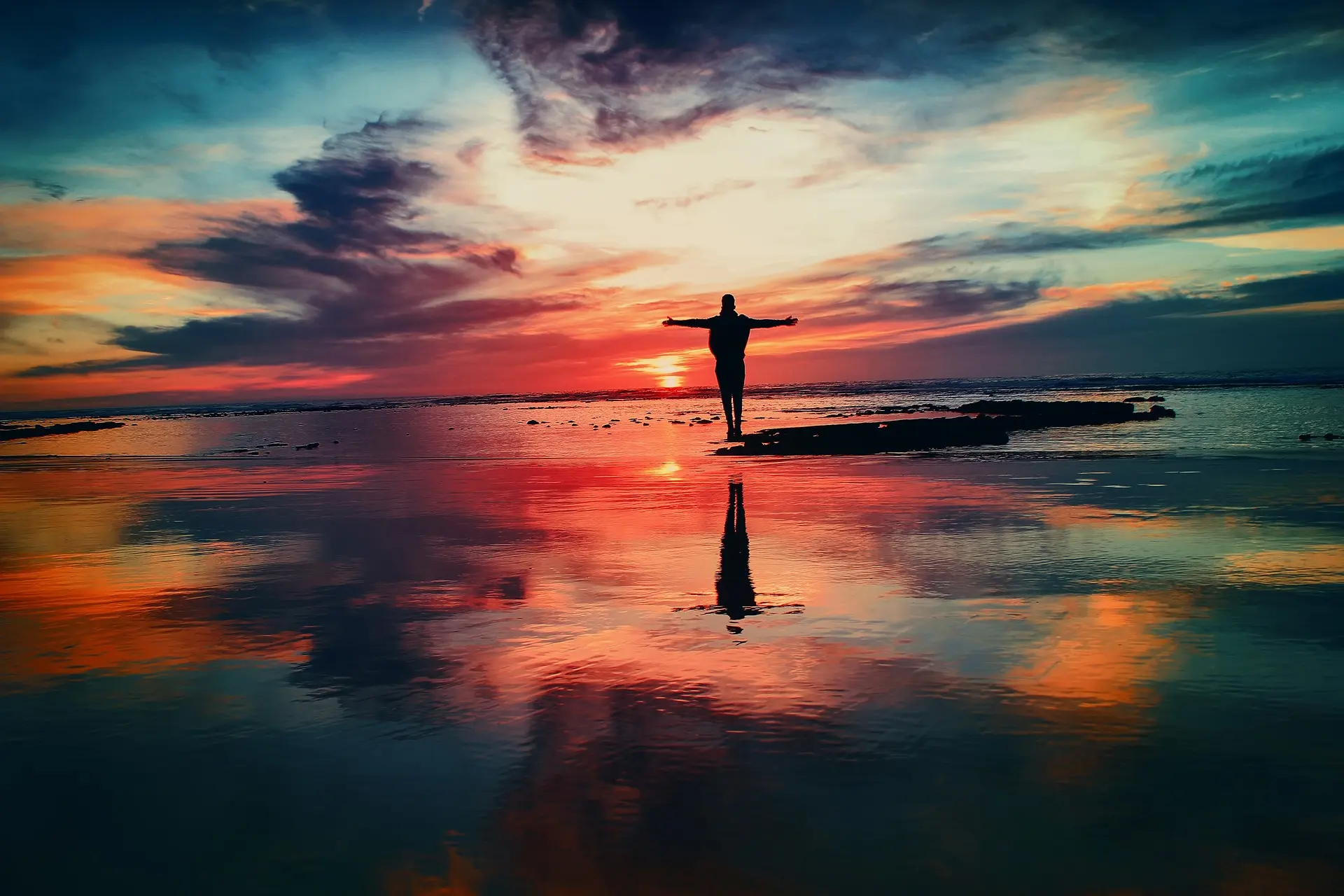 Man standing infront of the ocean with his arms spread out